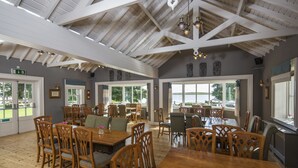 A spacious dining area with wooden tables and chairs, large windows offering views of the outdoors, and a high ceiling with exposed beams. - Lusty Beg Island (Enniskillen)