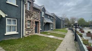 A row of modern houses with stone and dark siding, a paved walkway, and a grassy area with white flowers.