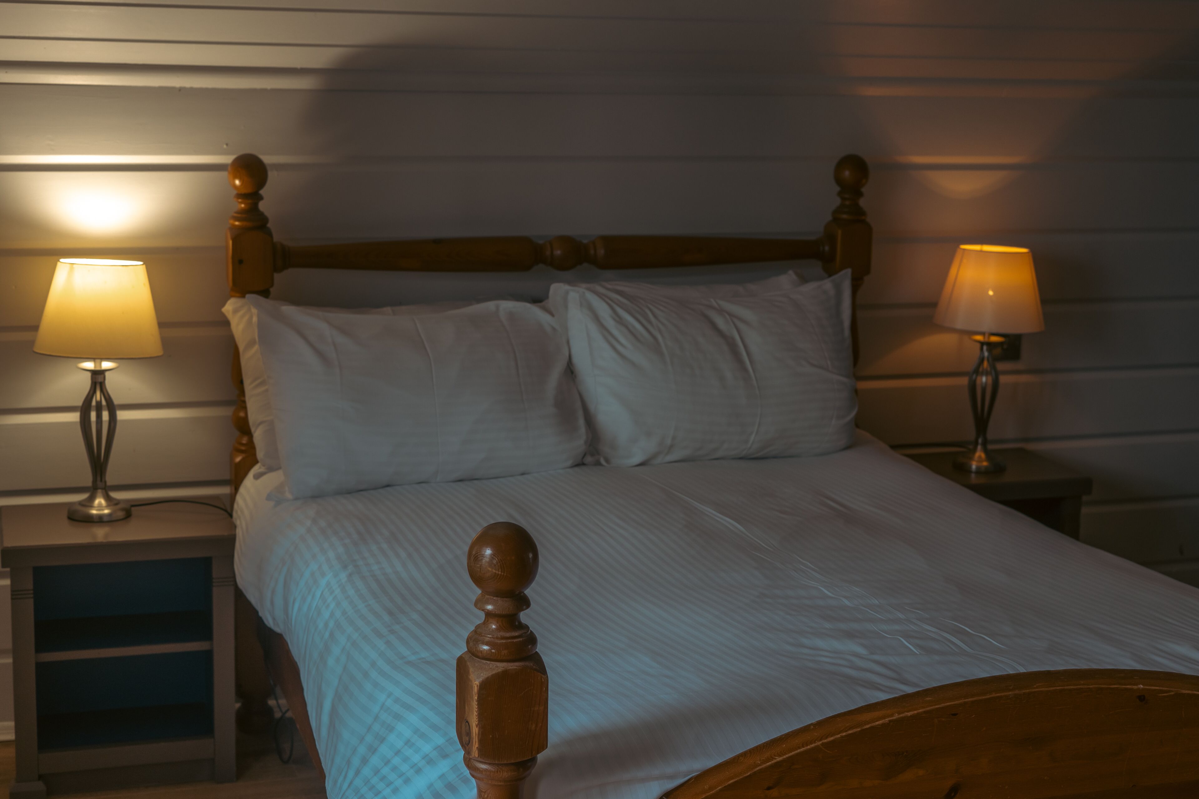A neatly made bed with a wooden headboard and two bedside lamps.