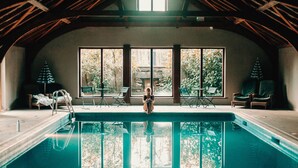 A pool area with a view of trees through large windows, a ladder, and lounge chairs. - Lusty Beg Island (Enniskillen)