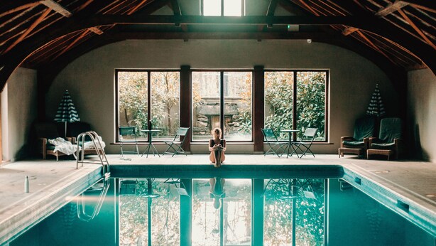 A pool area with a view of trees through large windows, a ladder, and lounge chairs. - Lusty Beg Island (Enniskillen)