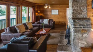 A cozy log cabin interior with a stone fireplace, wooden walls, and a seating area with a sofa and armchairs. - Lusty Beg Island (Enniskillen)