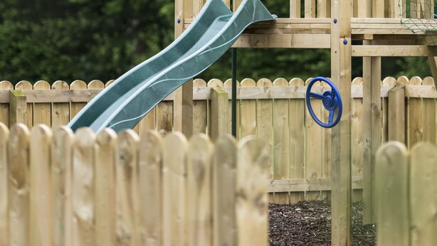 A wooden play structure with a slide and a small enclosed area, surrounded by a wooden fence. - Lusty Beg Island (Enniskillen)