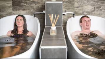 Two spa tubs with water and seaweed, a small container with reed sticks, and a stone wall background.