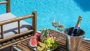 Een houten tafel met een fruitschaal, twee glazen witte wijn en een champagnefles.