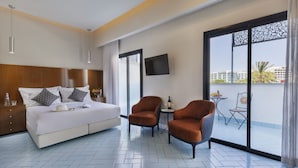 Ein modernes Hotelzimmer mit einem großen Bett, zwei Sesseln, einem kleinen Tisch mit Flasche und Gläsern sowie einem Fernseher an der Wand.