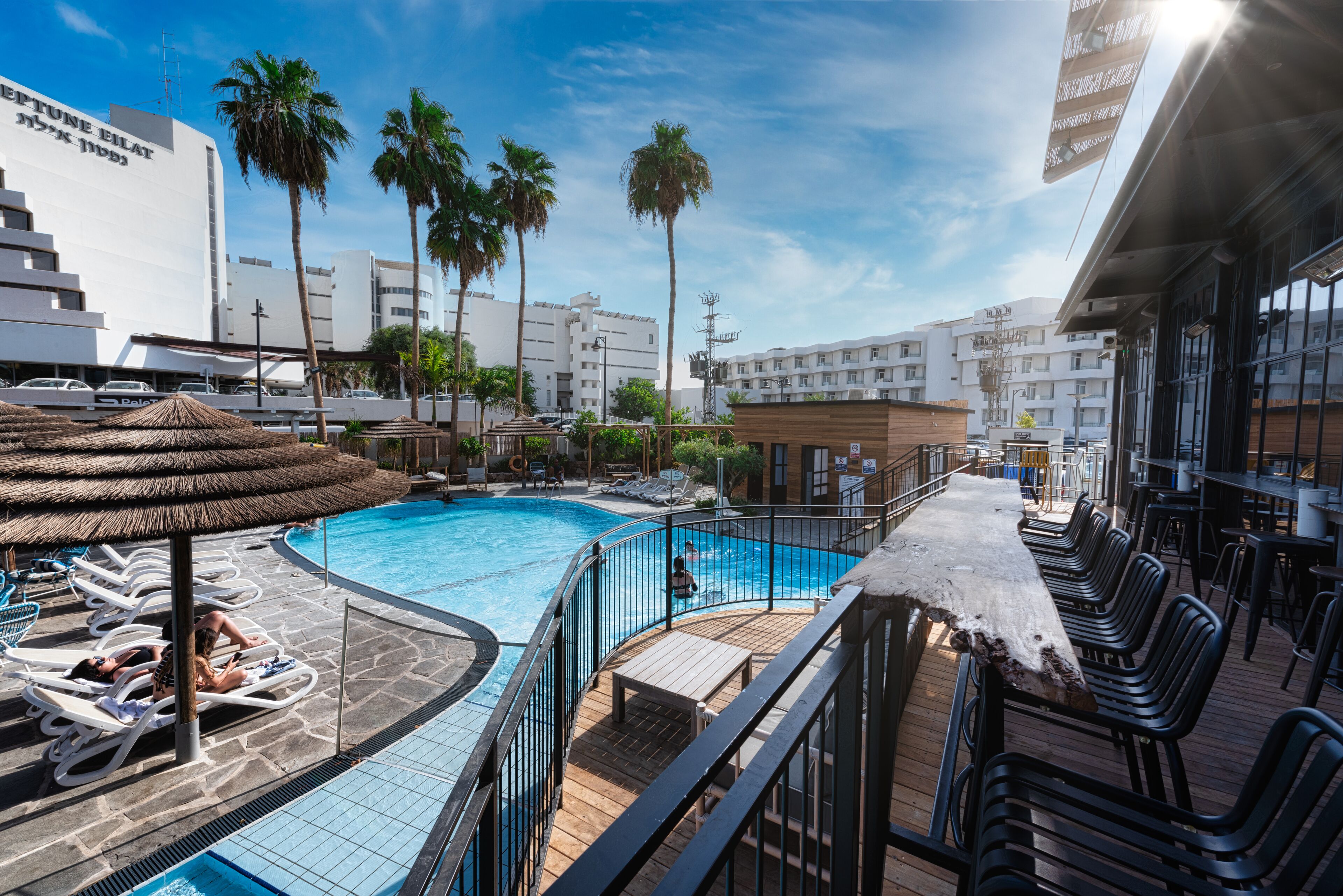 A pool area with lounge chairs, a wooden deck, and a bar area.
