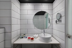 A modern bathroom with white tiles, a round mirror, a sink, and two small flower vases on the counter.