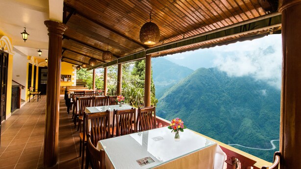 A restaurant with wooden tables and chairs, a view of a mountainous landscape, and a tiled floor. - SapaAubergeDangtrung Hotel (Sa Pa)
