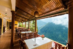 A restaurant with wooden tables and chairs, a view of a mountainous landscape, and a tiled floor. - SapaAubergeDangtrung Hotel (Sa Pa)