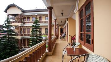 A hotel corridor with a covered balcony, wooden railings, and potted plants.