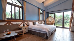 Quarto com cama, cadeira suspensa, sofá, mesa com copos e frutas, e janelas amplas com cortinas.