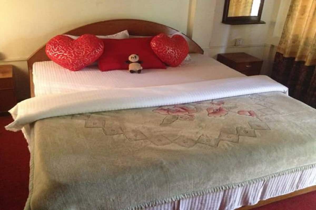 Ein ordentlich bezogenes Bett mit einem blumigen Überwurf und zwei roten herzförmigen Kissen.