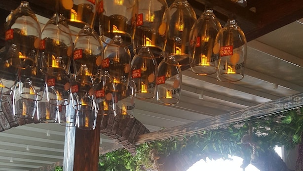 A restaurant interior with hanging glass bottles, brick walls, and wooden tables. - Nova Citrus Hotel (Seferihisar)