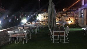 An outdoor dining area with tables and chairs, a stone wall, and a stone pillar. - Nova Citrus Hotel (Seferihisar)