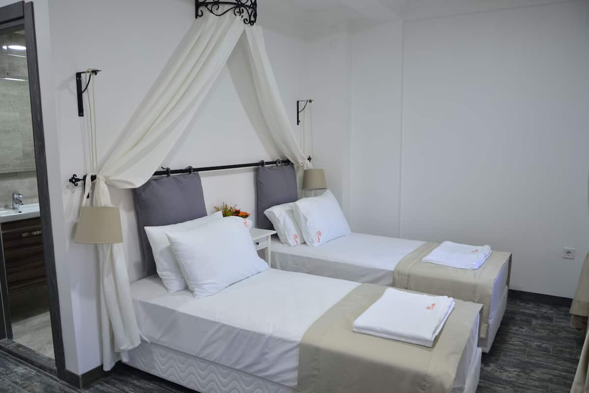 Une chambre d’hôtel avec deux lits, chacun doté d’un baldaquin, d’une table de chevet, d’une lampe et d’une petite table agrémentée d’un arrangement floral.
