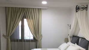 A neatly made bed with white linens and pillows, a bedside table with a lamp, and a window with curtains. - Nova Citrus Hotel (Seferihisar)