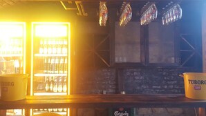 A bar area with a beer tap, a carlsberg sign, and a tuborg bucket. - Nova Citrus Hotel (Seferihisar)