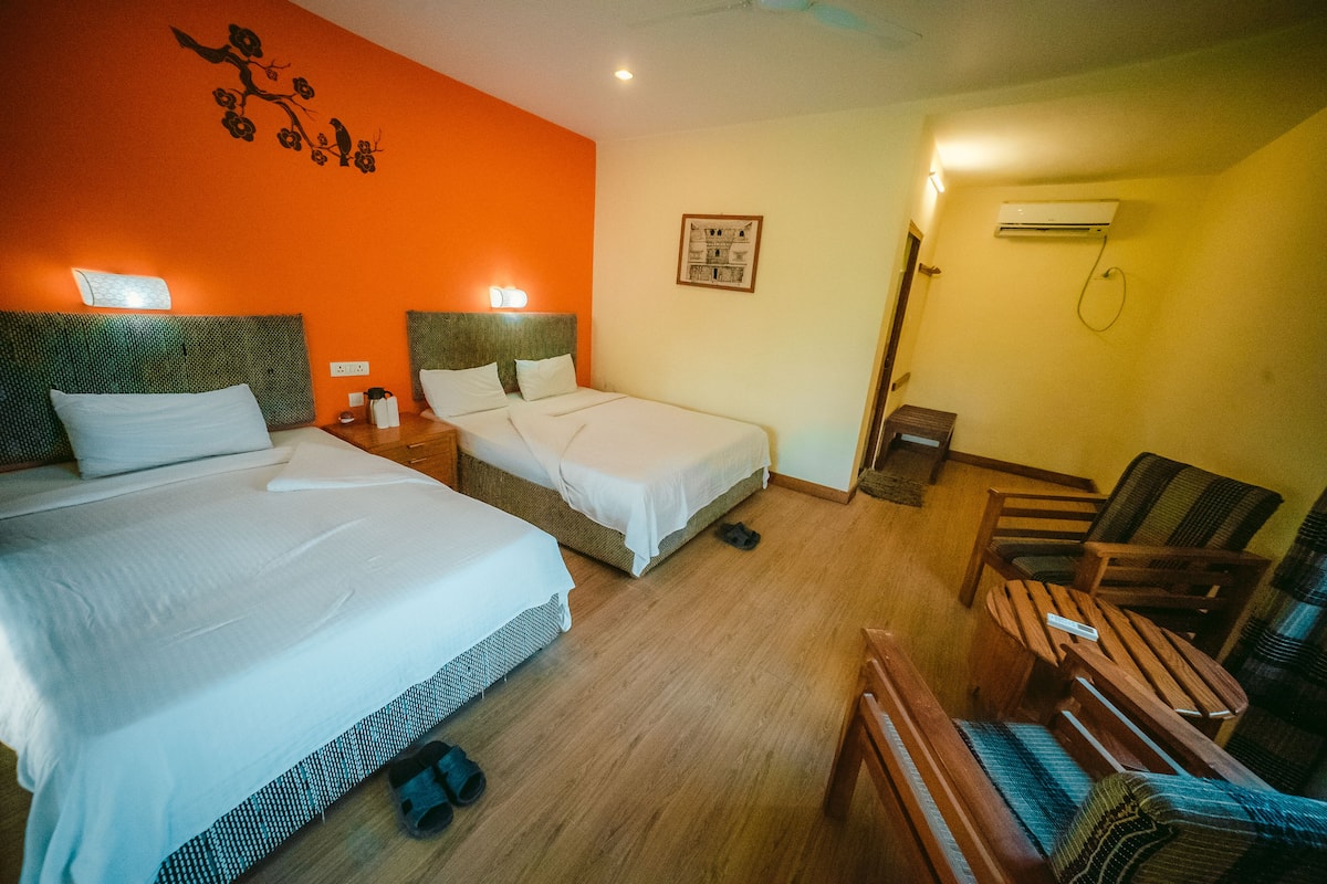 A hotel room with two beds, a chair, a small table, and an air conditioning unit.