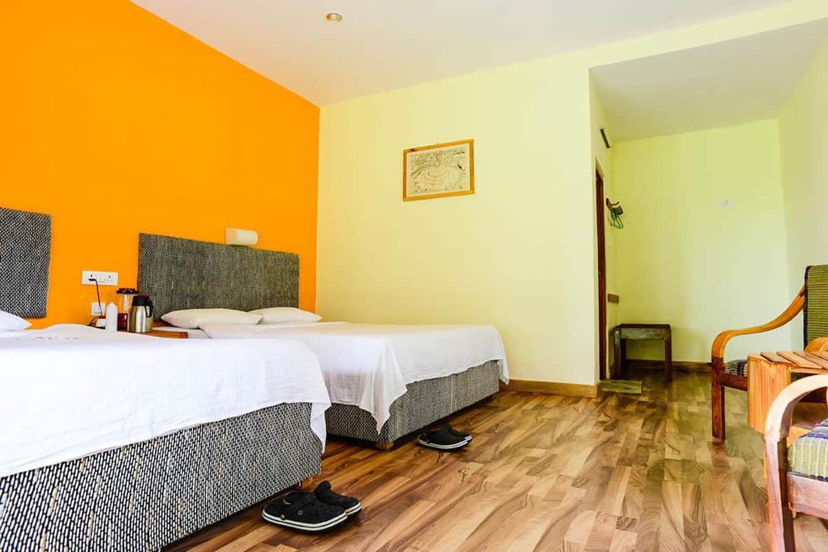 A hotel room with two beds, a wooden floor, and a chair.