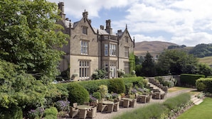 A large, historic stone building with multiple windows and a well-maintained garden with outdoor seating. - Falcon Manor Hotel (Settle)