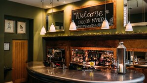 A bar area with a curved counter, a welcome sign, framed artwork, and a mirror above the bar. - Falcon Manor Hotel (Settle)