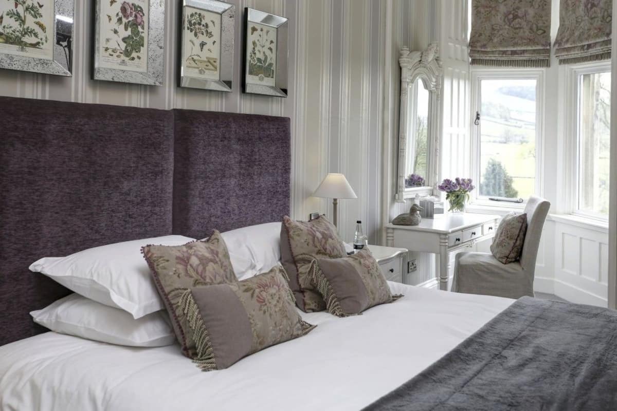 A bedroom with a large bed, a nightstand, a chair, and a window with a view.