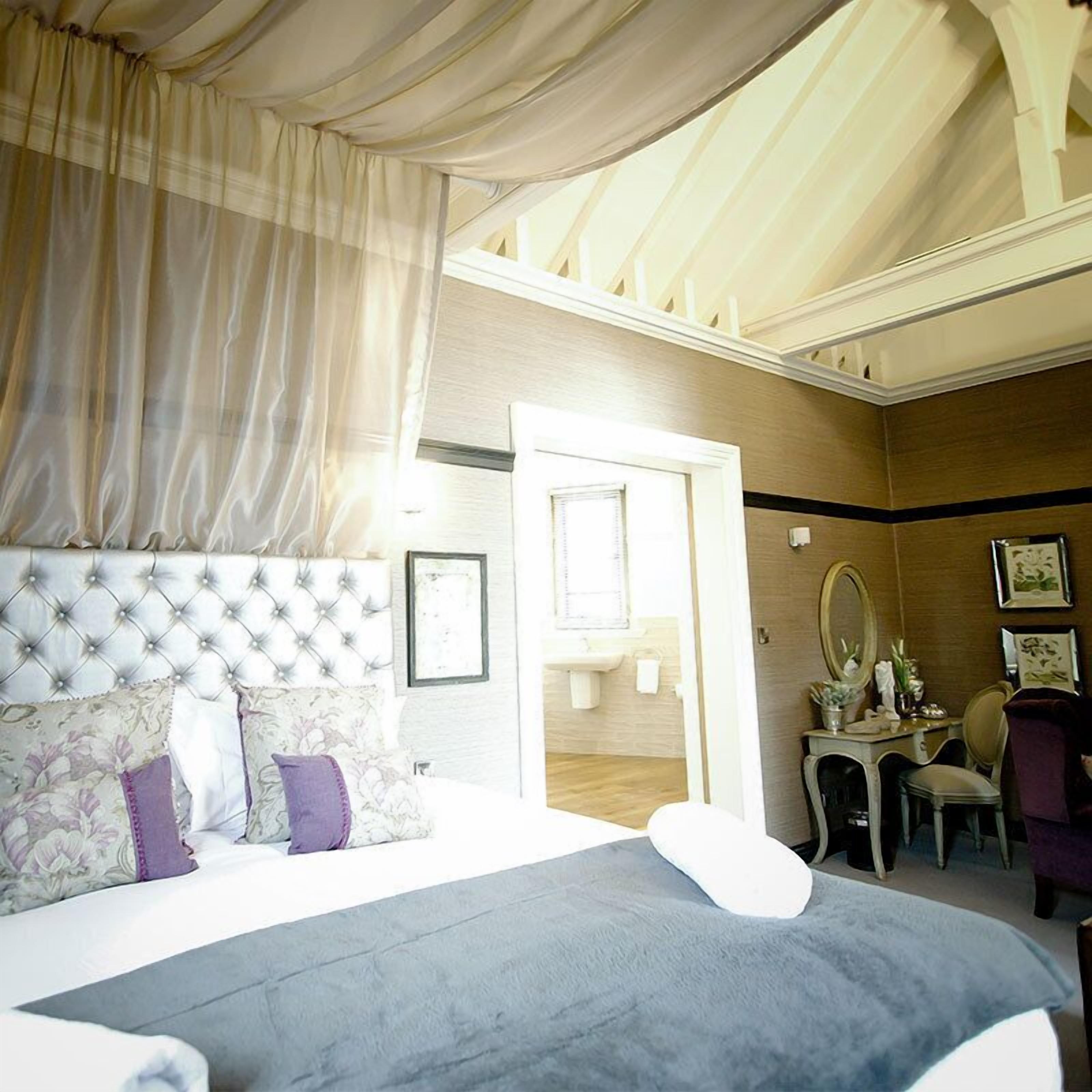 A bedroom with a large bed, a vanity with a mirror, and a door leading to a bathroom.