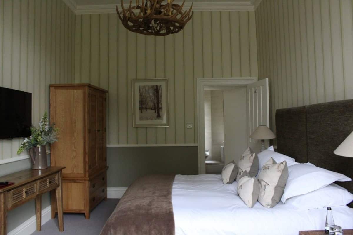 A bedroom with a large bed, a wooden wardrobe, a television, and a chandelier.
