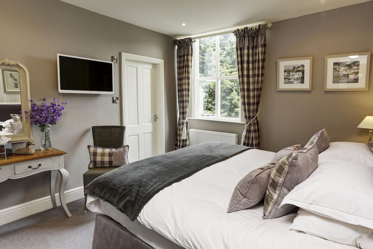 A bedroom with a bed, a desk, a chair, a TV, and a window with curtains.
