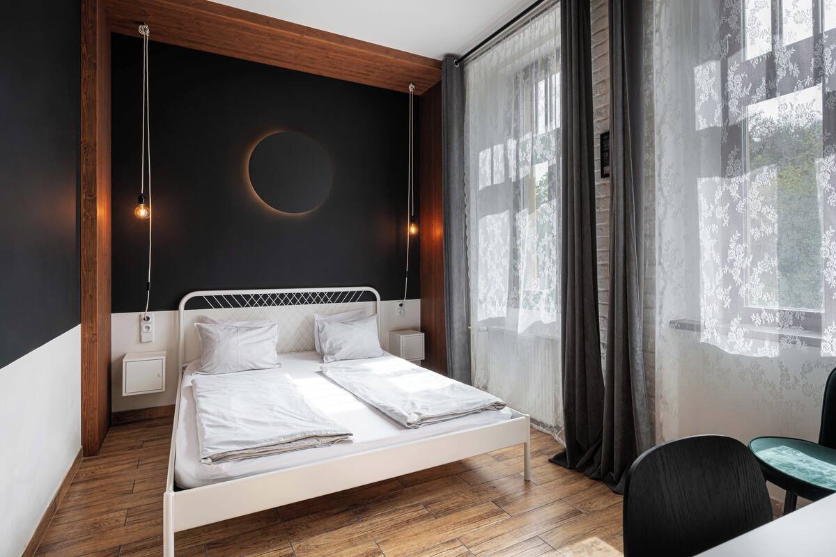A modern bedroom with a bed, bedside tables, and a view of the outdoors through sheer curtains.