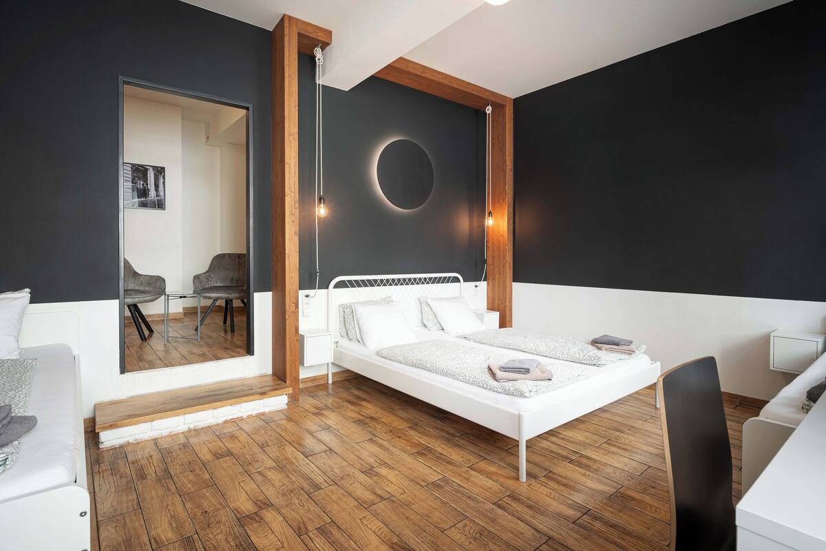 A modern bedroom with a white bed, wooden floor, and a large mirror.