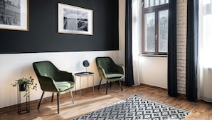 A modern room with two green armchairs, a small table, and a potted plant. There are two framed pictures on the wall and a window with curtains. - Bohem Prague Hotel (Prague)