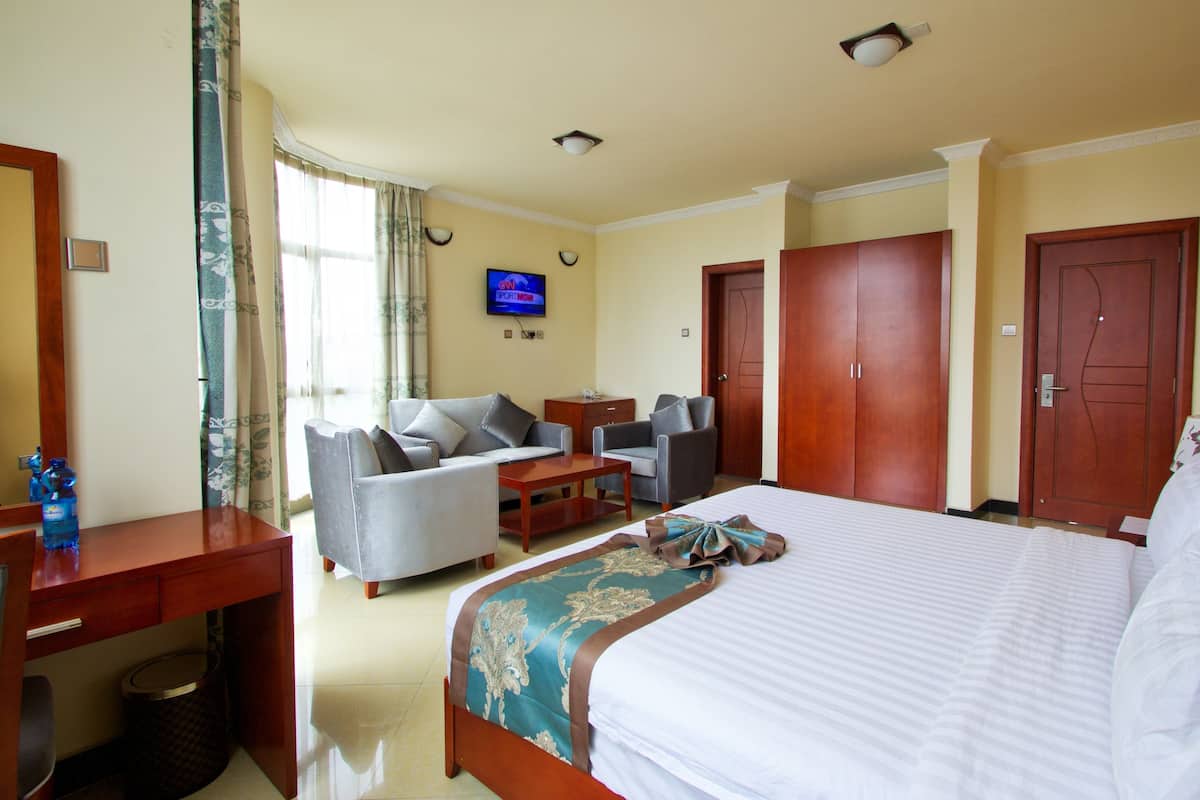 Quarto de hotel com cama, duas poltronas, escrivaninha, televisão e guarda-roupa.