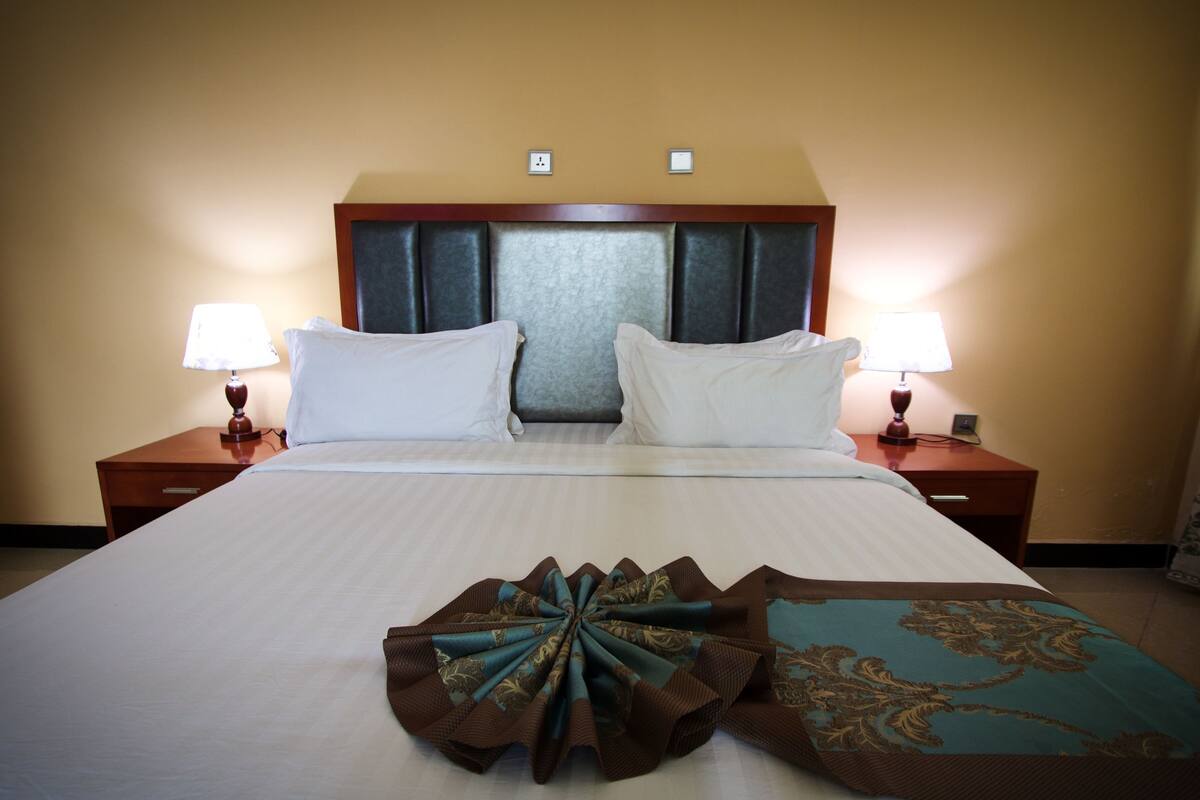 Quarto de hotel com uma cama grande, duas mesas de cabeceira e duas luminárias.