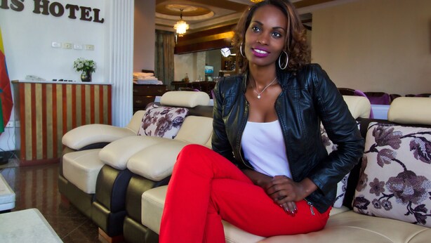 A woman sitting on a sofa in a hotel lobby with a sign reading "Heritage Hotel" in the background. - Hera Addis Hotel (Addis Ababa)