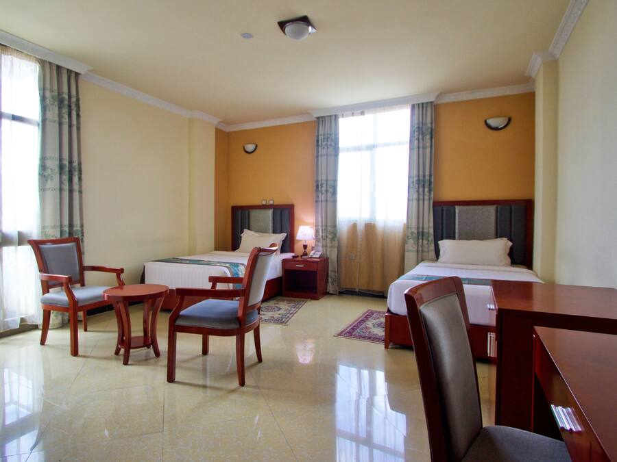 A hotel room with two beds, a desk, and two chairs.