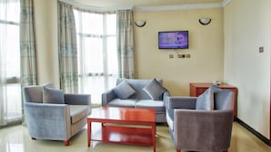 A living room with a sofa set, a coffee table, a TV mounted on the wall, and a telephone on a side table. - Hera Addis Hotel (Addis Ababa)