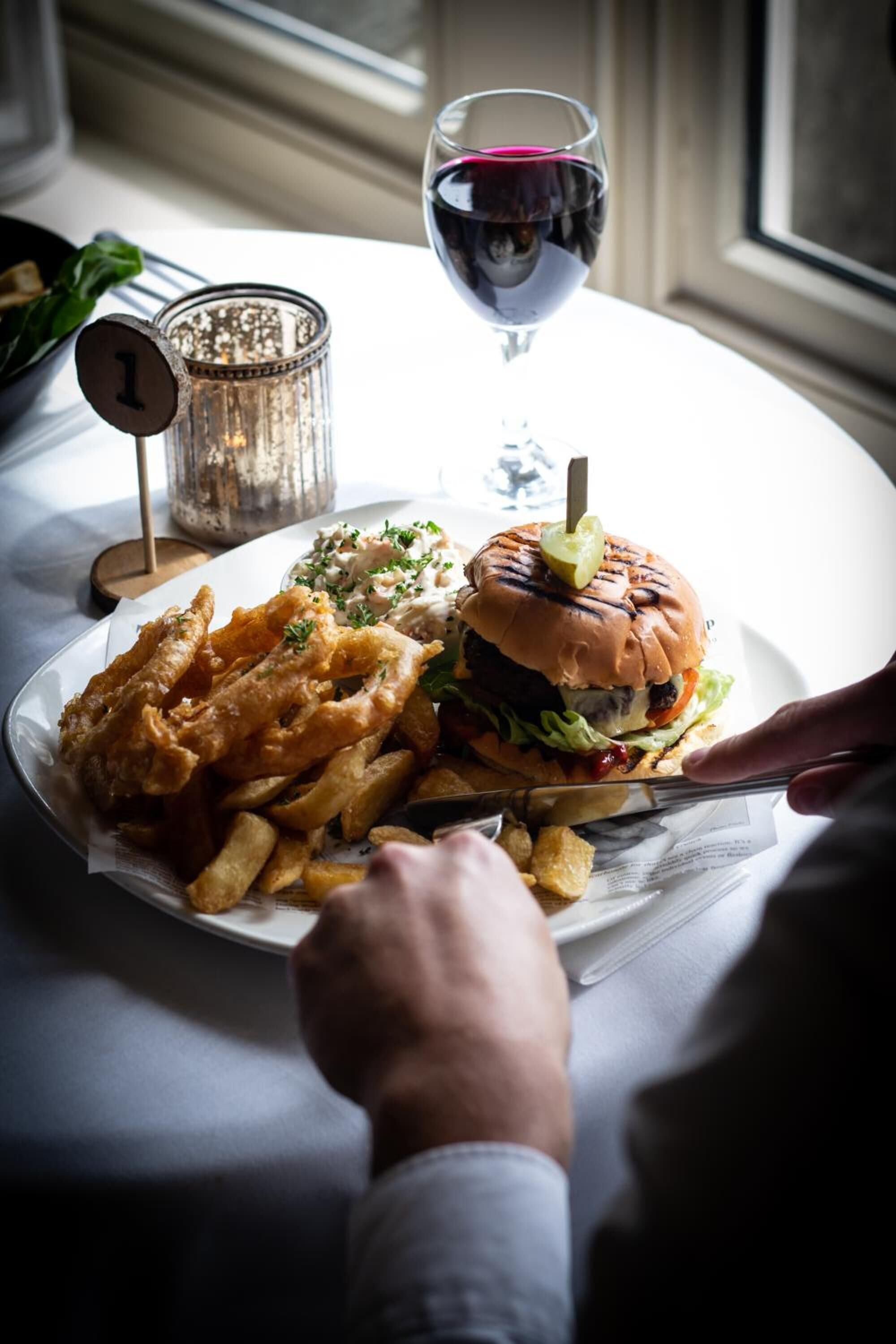 Een bord met een hamburger, friet en een glas rode wijn op een tafel.