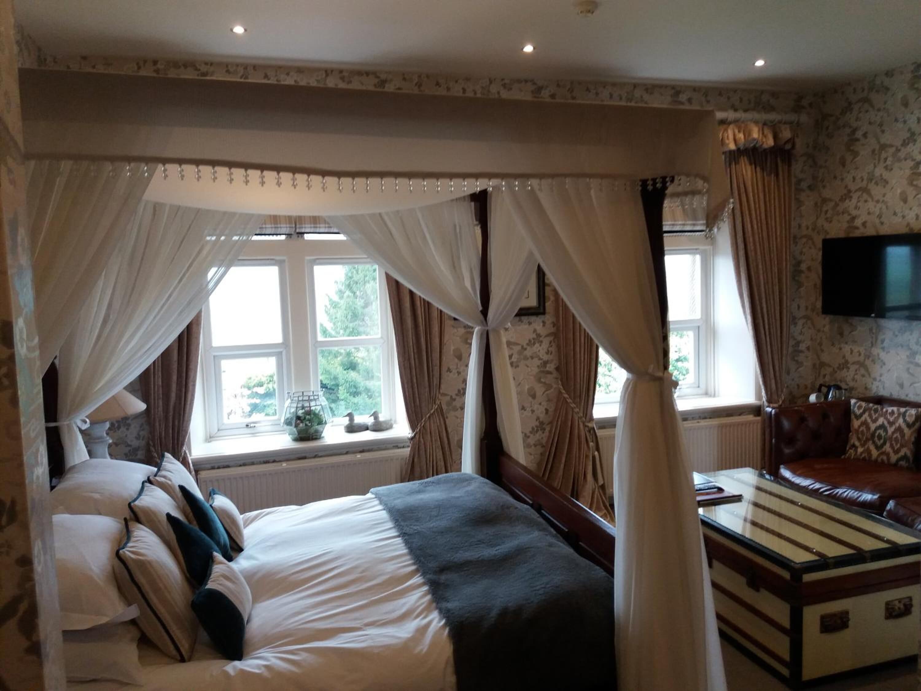 A bedroom with a four-poster bed, a television mounted on the wall, and a window with curtains.