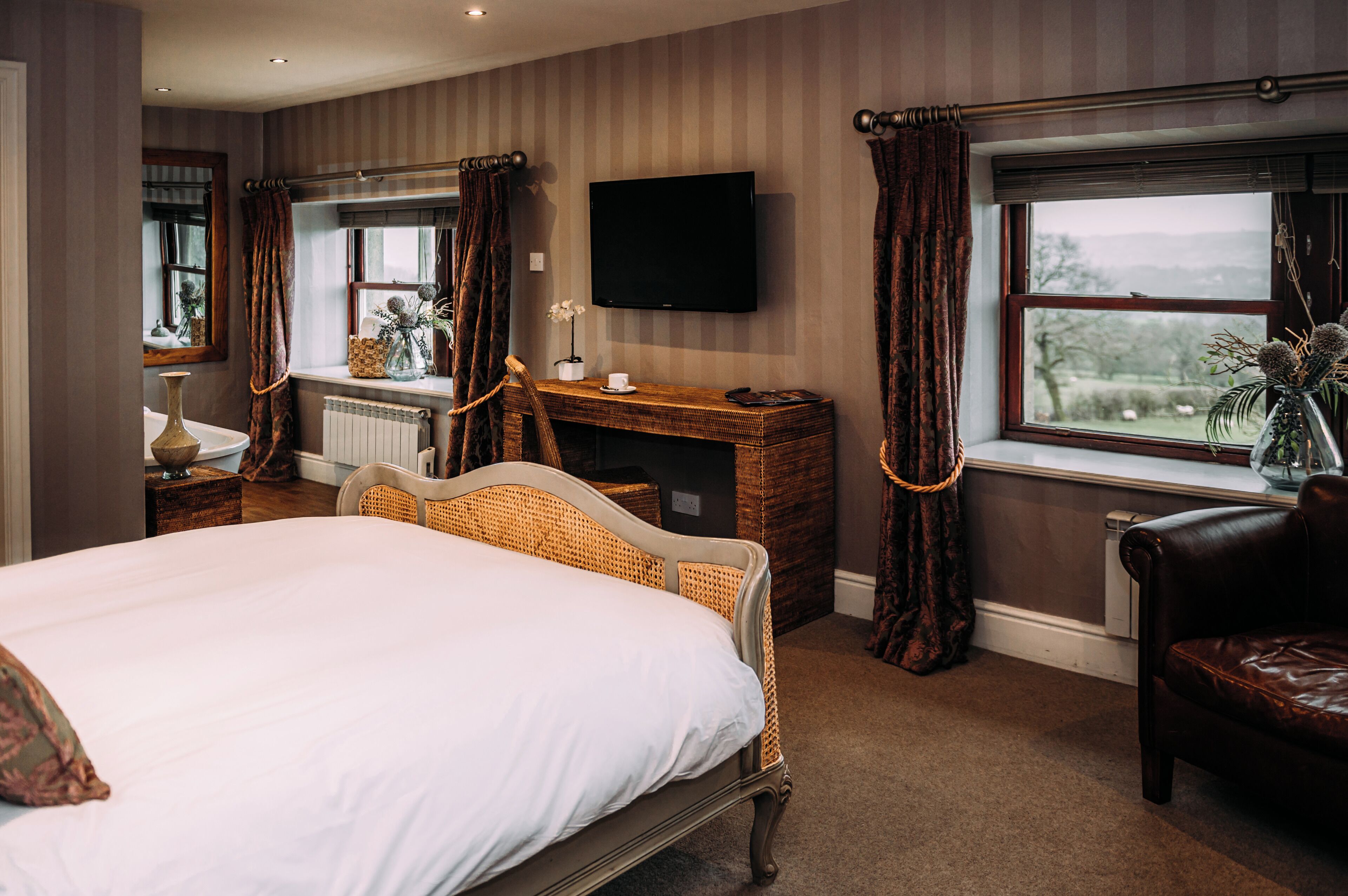 A bedroom with a large bed, a dresser, a TV mounted on the wall, and a view of the outdoors through a window.