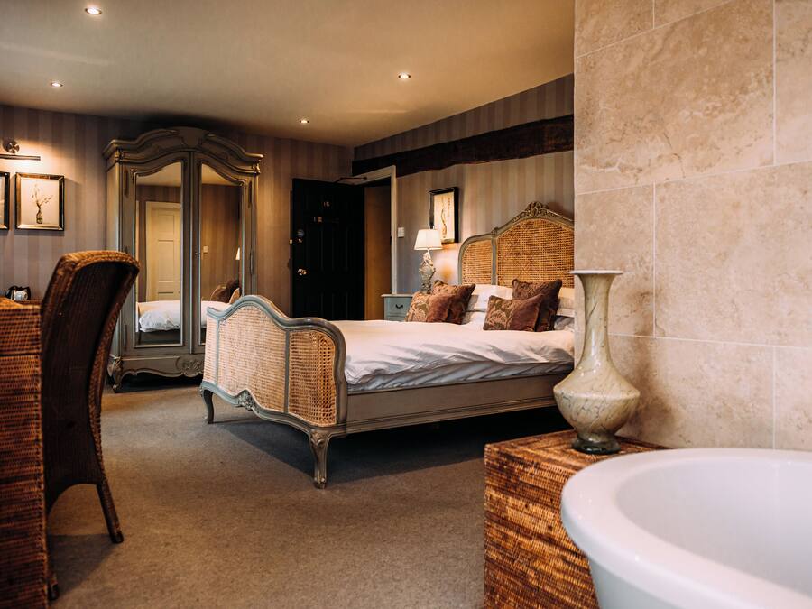 A bedroom with a four-poster bed, a large mirror, a nightstand with a lamp, and a bathtub.