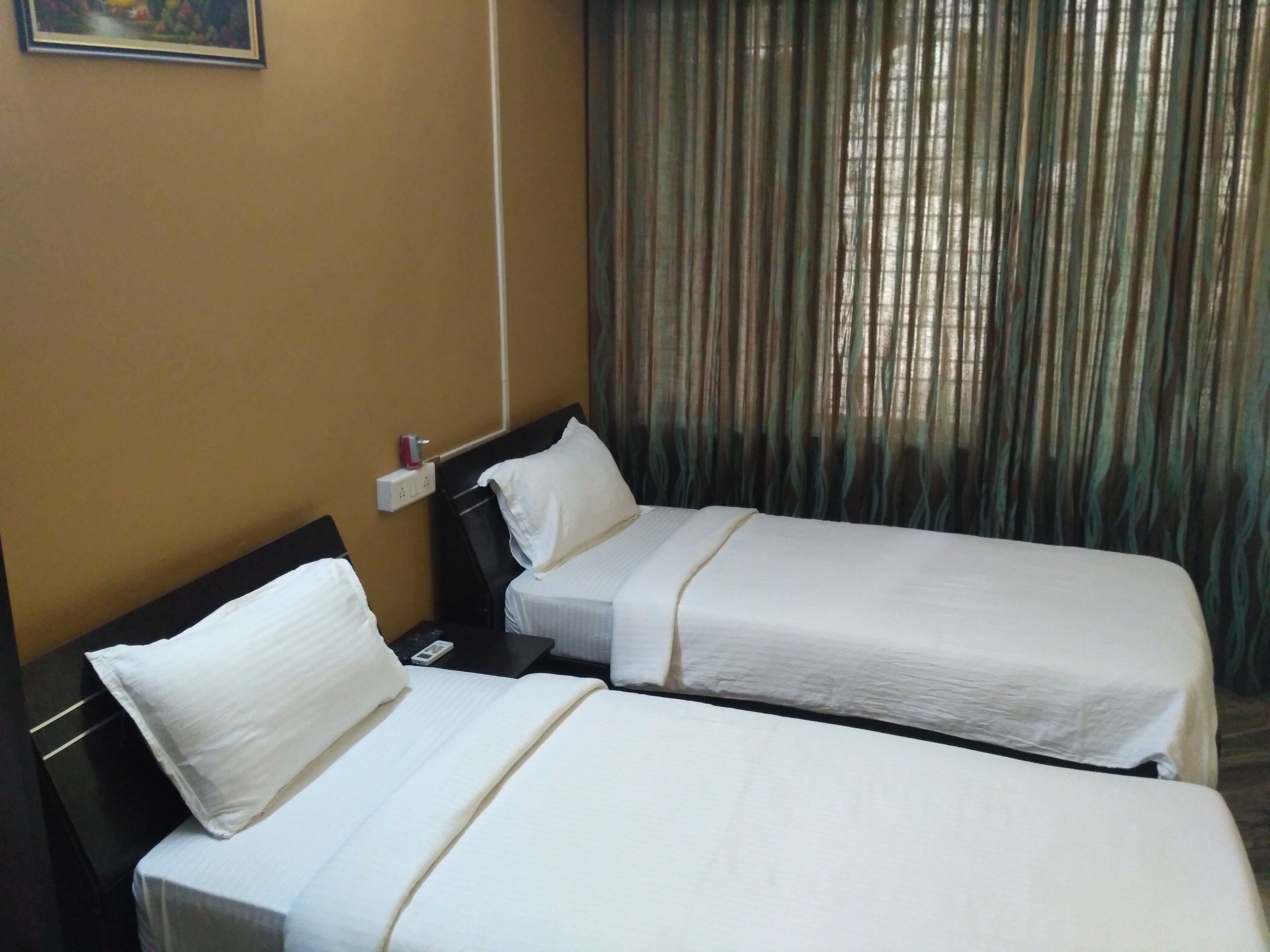 Habitación de hotel con dos camas individuales, una mesita de noche, un enchufe y una ventana con cortinas.