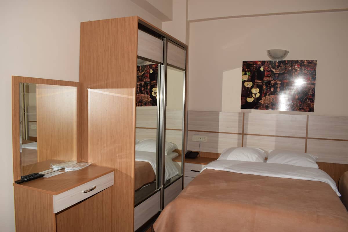 Ein Hotelzimmer mit einem Holzschrank, einem Nachttisch mit Fernbedienung, einem Bett mit weißer Bettwäsche und einem an der Wand befestigten Spiegel.