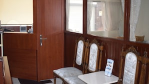 Una habitación con puerta de madera, una ventana con cortinas, una mesa y dos sillas tapizadas.