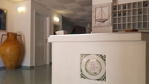 A hallway with a white reception desk, a large vase, and a wall-mounted light fixture. - Hotel del Molo (Palau)