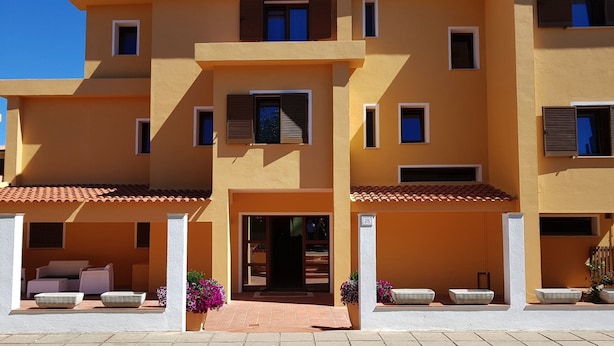 A multi-story building with a yellow facade, multiple windows with shutters, and a tiled roof. - Hotel del Molo (Palau)