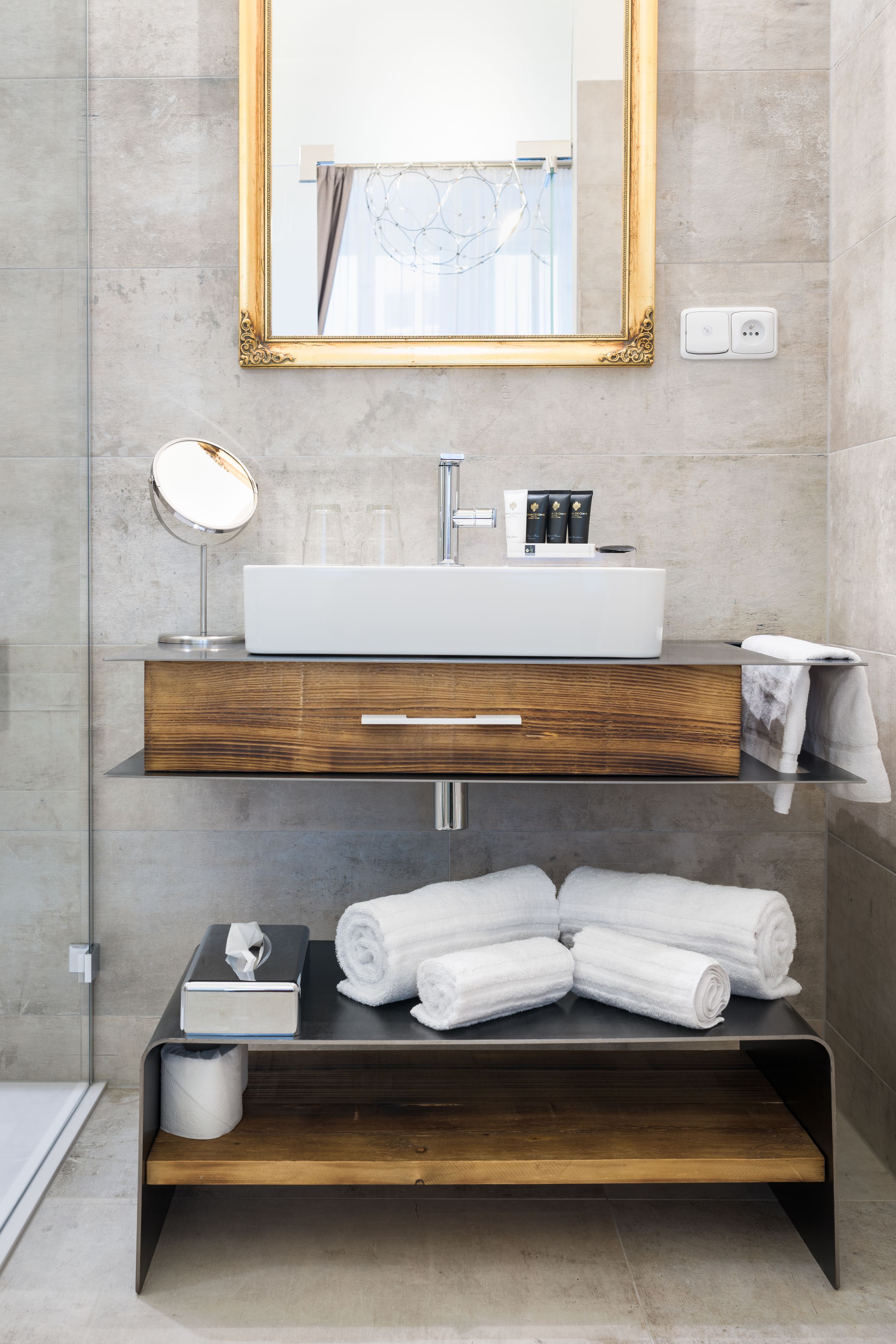 A modern bathroom with a large mirror, a white sink, a wooden vanity, and neatly rolled towels.