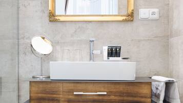 A modern bathroom with a large mirror, a white sink, a wooden vanity, and neatly rolled towels.