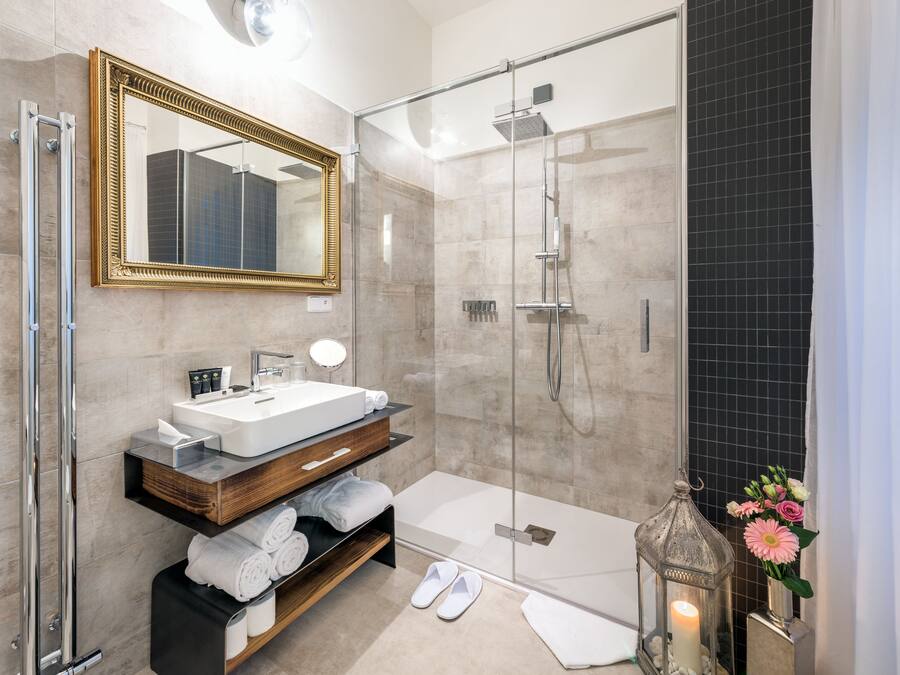 Un baño moderno con ducha acristalada, un espejo grande, un mueble de tocador de madera y un farol decorativo.